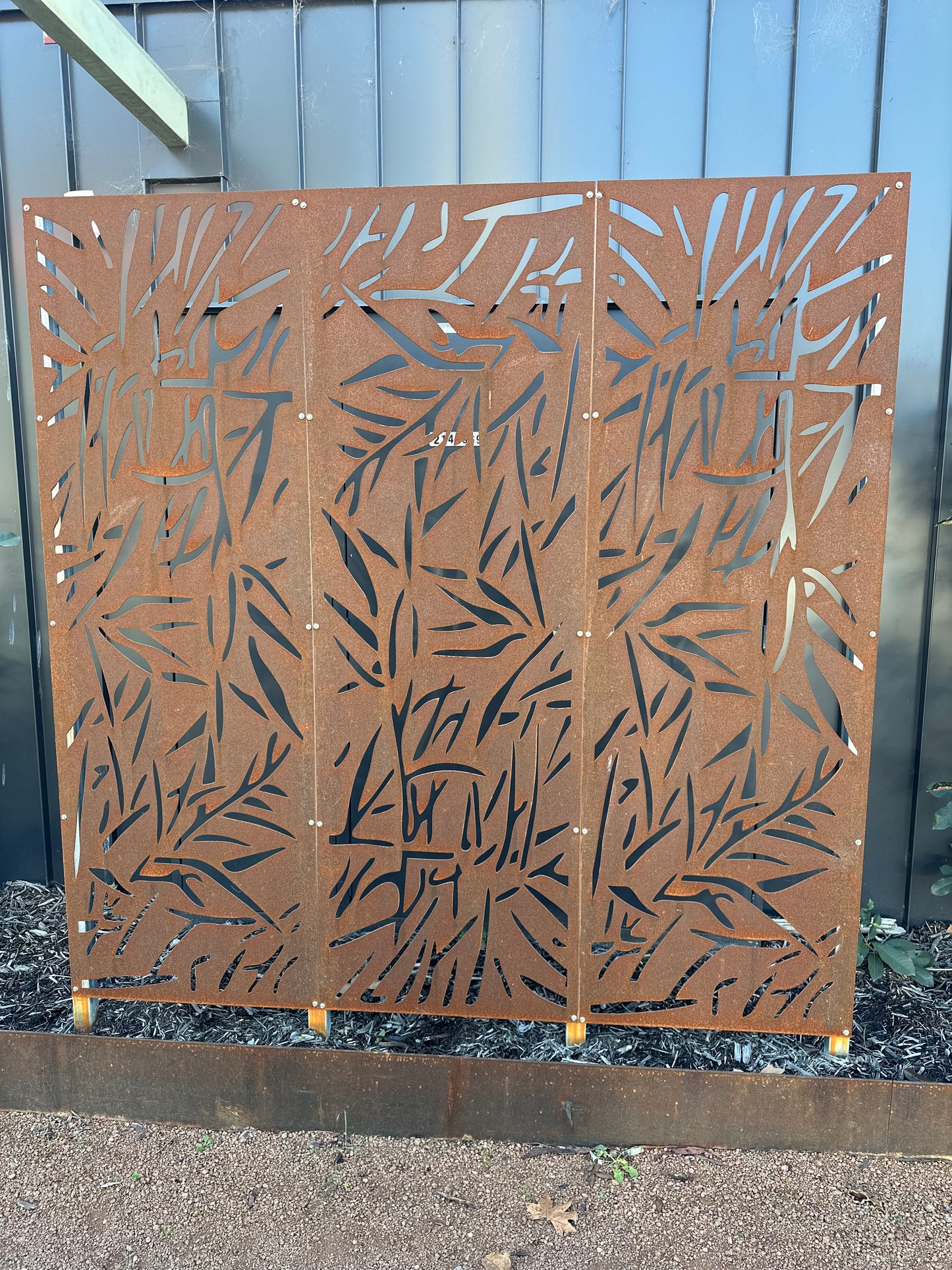 Three-panel corten steel privacy screen with laser-cut decorative design, creating a striking focal point and added privacy in a landscaped garden setting.