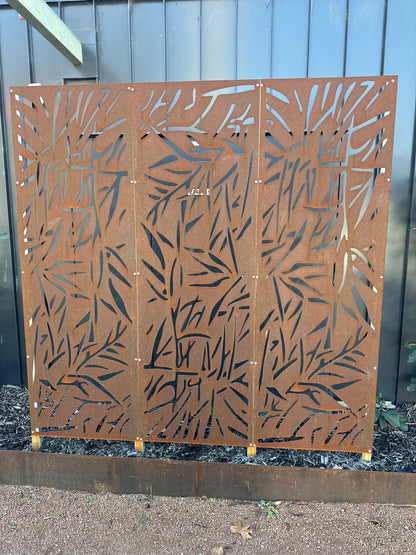 Three-panel corten steel privacy screen with laser-cut decorative design, creating a striking focal point and added privacy in a landscaped garden setting.